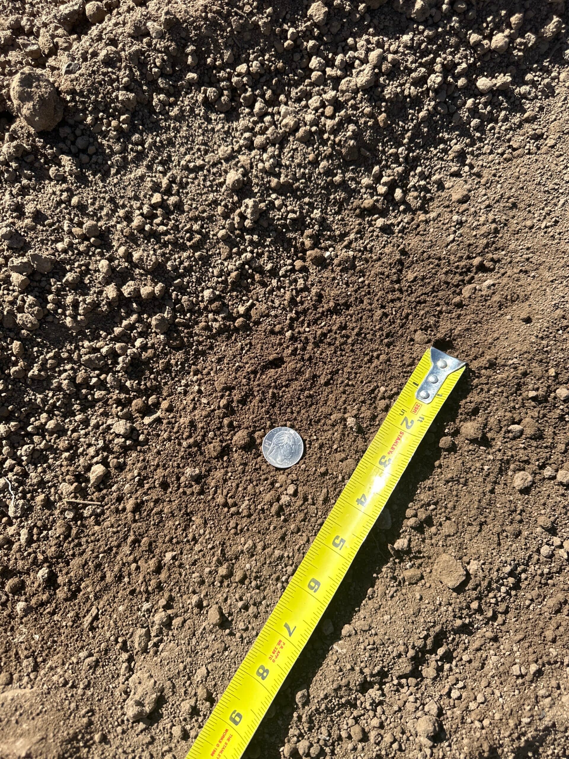 Darby Pit, Gravel & Trucking - We specialize in supplying top-quality materials such as dirt, sand, gravel, and crushed stone. Additionally, we offer comprehensive trucking services to meet the needs of excavation projects, landscaping endeavors, home builders' requirements, and the construction of roads, paths, driveways, and foundations. Our Screened Topsoil is a testament to our commitment to quality; a coin and a yellow tape measure lie on its rich brown surface, underscoring its superior condition.