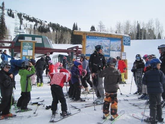 Teton Valley Non-Profits, A group of individuals clad in ski gear gather on a snow-blanketed slope, adjacent to a ski lift and an information board. Majestic trees and towering mountains frame the scene, underscoring the Community Foundation of Teton Valley's commitment to supporting local non-profits and businesses through charitable giving. This picturesque setting symbolizes the foundation's efforts to foster community cohesion, ensuring resources are available to enhance both recreational facilities and essential services that benefit all residents. The Tin Cup Challenge & Run is the CFTV annual giving event day.