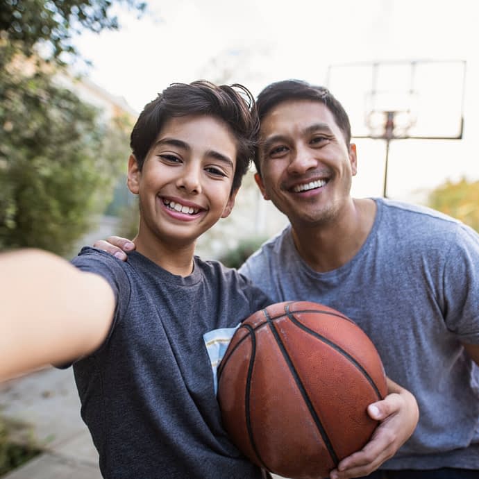 Hispanic father and son taking a selfie outdoors whilst playing basketball
