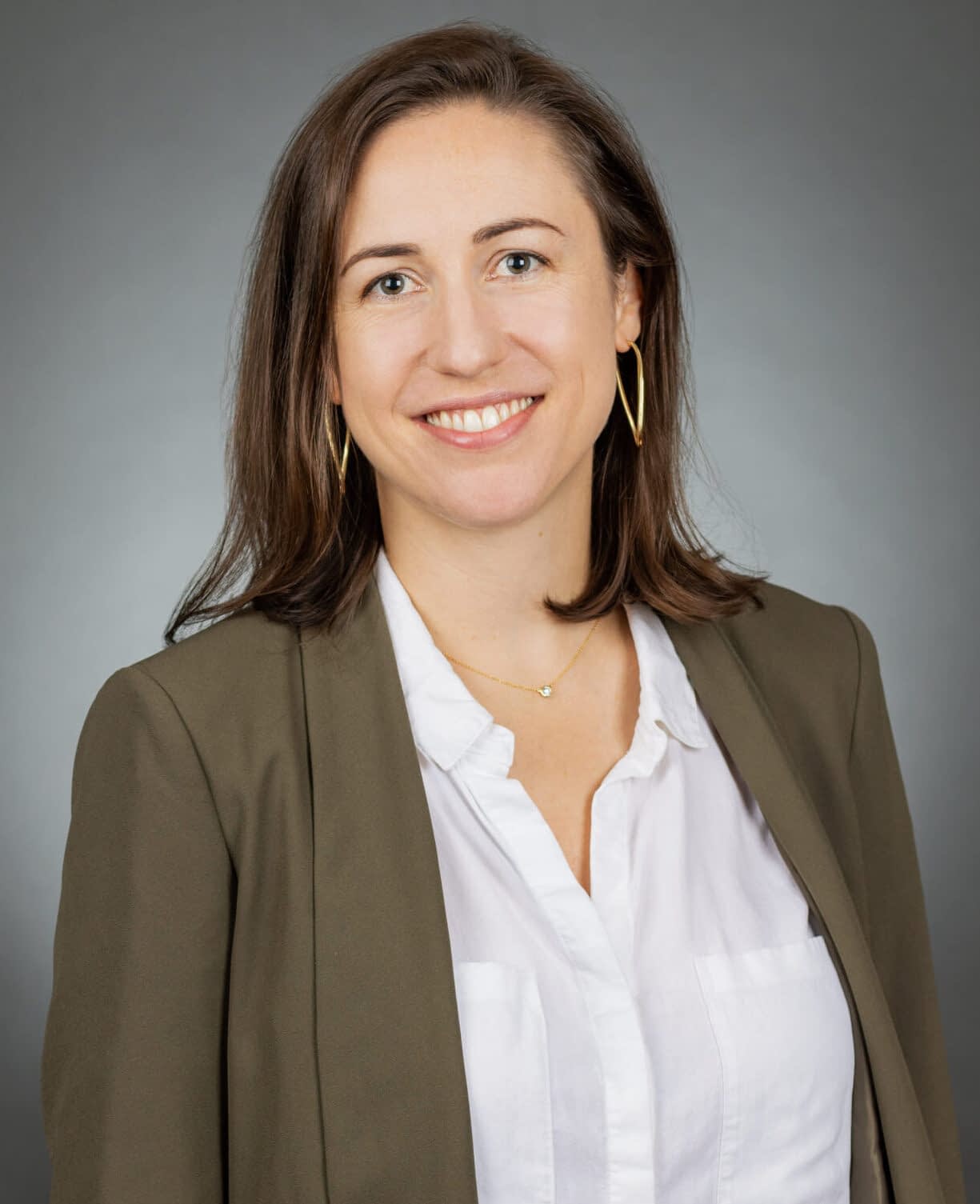 A person is wearing a collared shirt and outerwear, with a smile on their face, in an indoor headshot portrait.