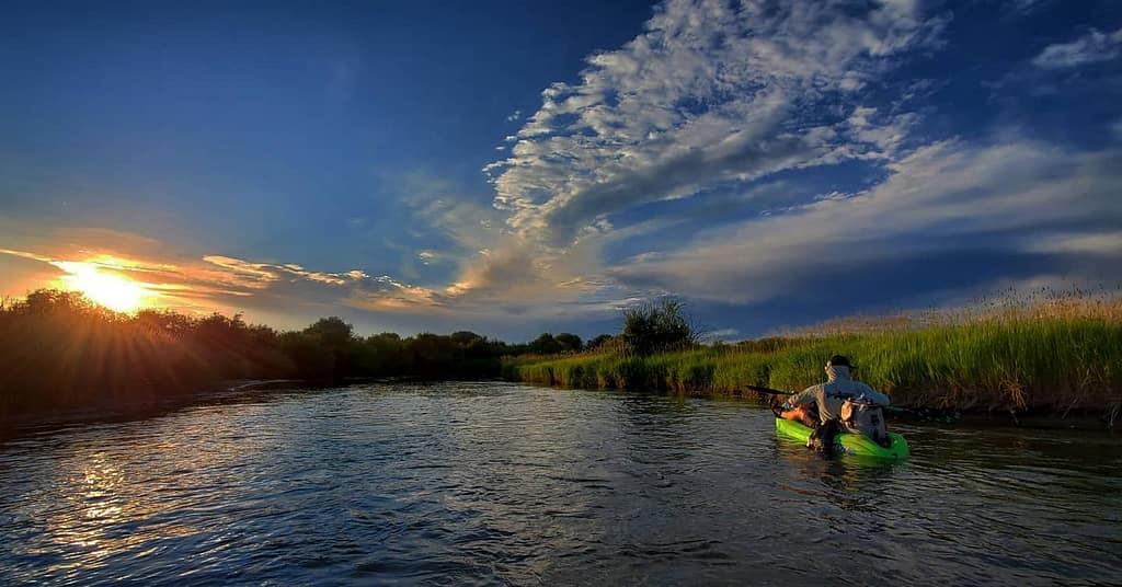 Kayakers on a calm river below a big evening sky